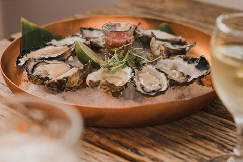 A close-up of a styled bowl of fresh oysters in their shells on a wooden table