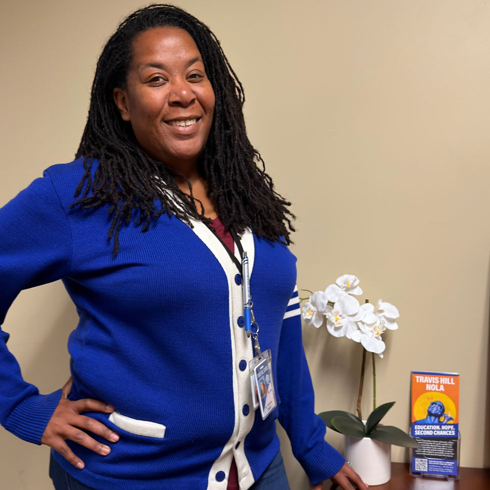 Smiling woman in a blue cardigan stands beside a table with white orchids and a colorful sign reading "Travis Hill NOLA" on a beige background.