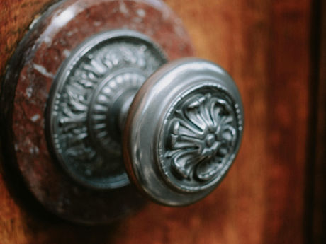 Ornate, metallic doorknob with floral design on wooden door; rich brown tones and intricate patterns evoke a vintage feel.