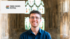 Matthew Elderton-Lewis standing in Gloucester Cathedral with Three Choirs Festival logo beside him