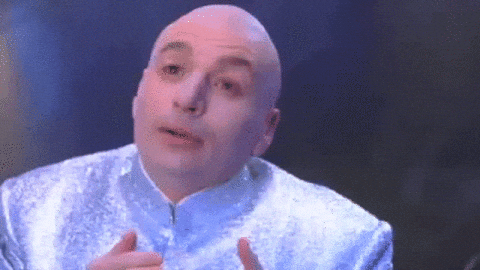 Bald man in a shiny silver suit speaks against a dark blue background, looking earnest.