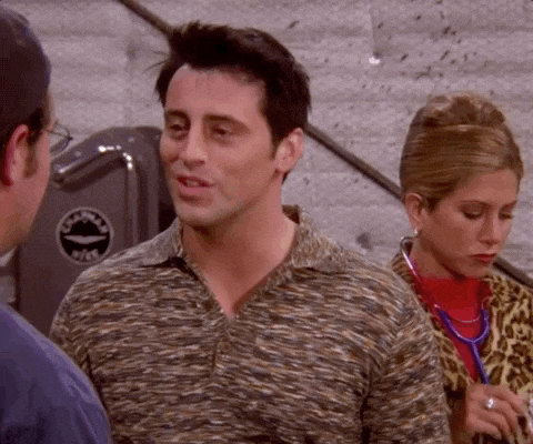 Man in patterned shirt talks to another man while a woman in leopard print looks down in an indoor room.