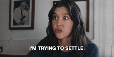 Woman speaking with determined expression says "I'm trying to settle." Indoor setting with a framed photo on the wall.