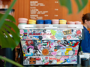 Sticker-covered espresso machine with colourful ceramic cups on a marble counter inside a contemporary specialty coffee shop in Zurich