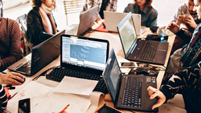 Professionnels de l’immobilier utilisant des ordinateurs portables, des documents et des ressources numériques partagées pour coordonner des tâches et examiner des informations lors d’une séance de planification collaborative