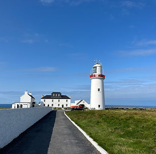 A Loop head lighthouse with ocean next to it and a cottage 