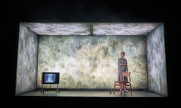 Theatre Lighting Programmer London a woman stands next to a chair in front of a wall with a picture of a man on it