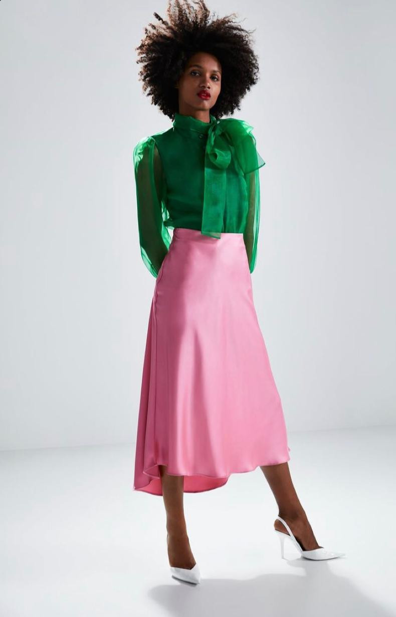 mulher negra com blusa transparente verde e saida midi rosa