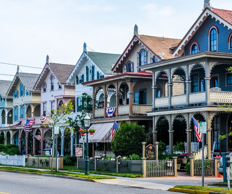 Row of colorful Victorian houses with intricate trim, American flags, and summer decor. Sunny day, peaceful suburban street.
