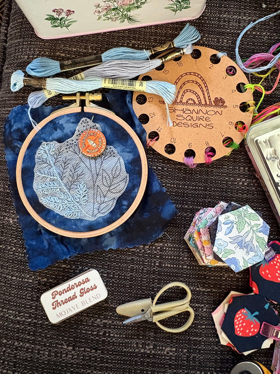 a bevy of crafts on a couch, including our cyanotype botanical samplers, thread, a thread keeper, and some english paper piecing