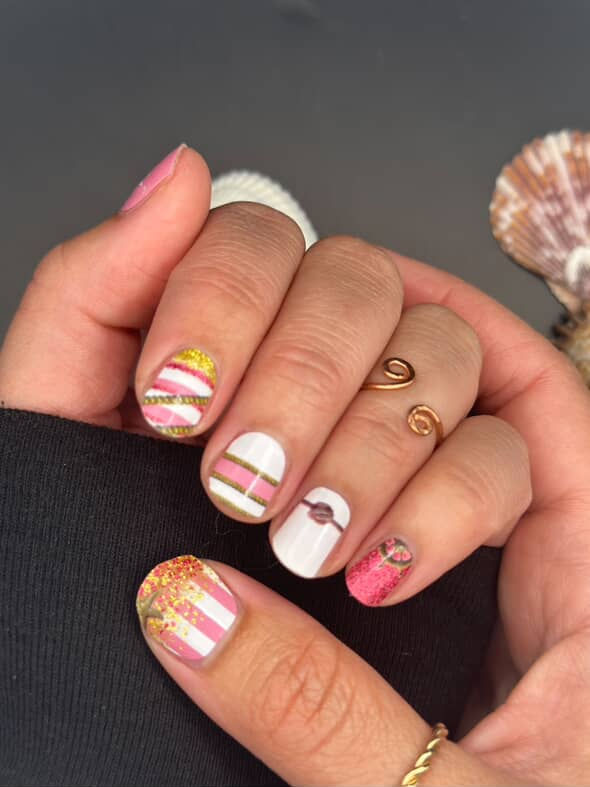 Model wearing Dockside Glam pink and gold nautical nail wraps with glitter, anchors, rope stripes, and starfish accents.