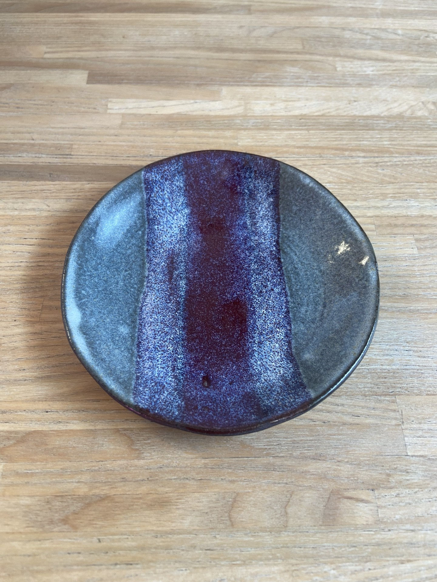 Handcrafted ceramic dish with earthy blue-grey tones and a plum glaze stripe, styled on natural wood.