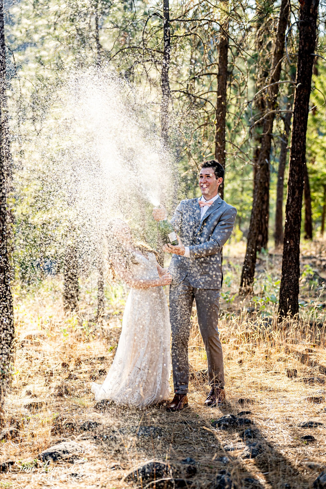 a couple pops a bottle of champagne with the liquid spraying to celebrate their elopement