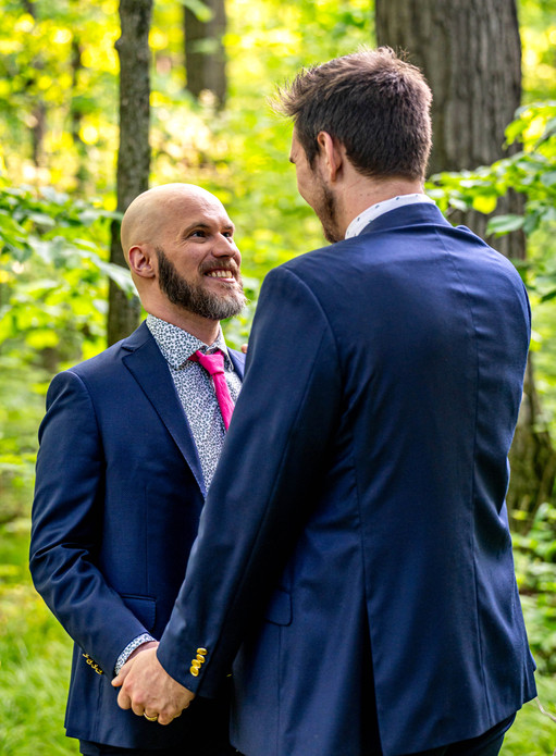 two men smile at each other, ones back is to the camera, the other is looking up loving into his husbands eyes