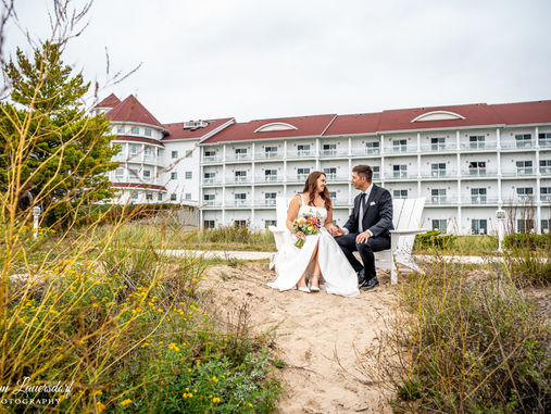 a newlywed couple sits in white chairs in front of Blue Harbor Resort in Sheboygan