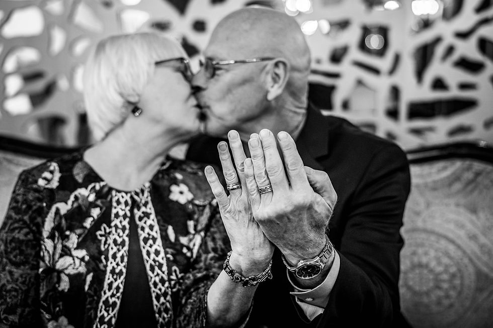 Elderly couple kissing, showing their wedding rings. Black and white image with abstract patterns in the background. Romantic and joyful mood.