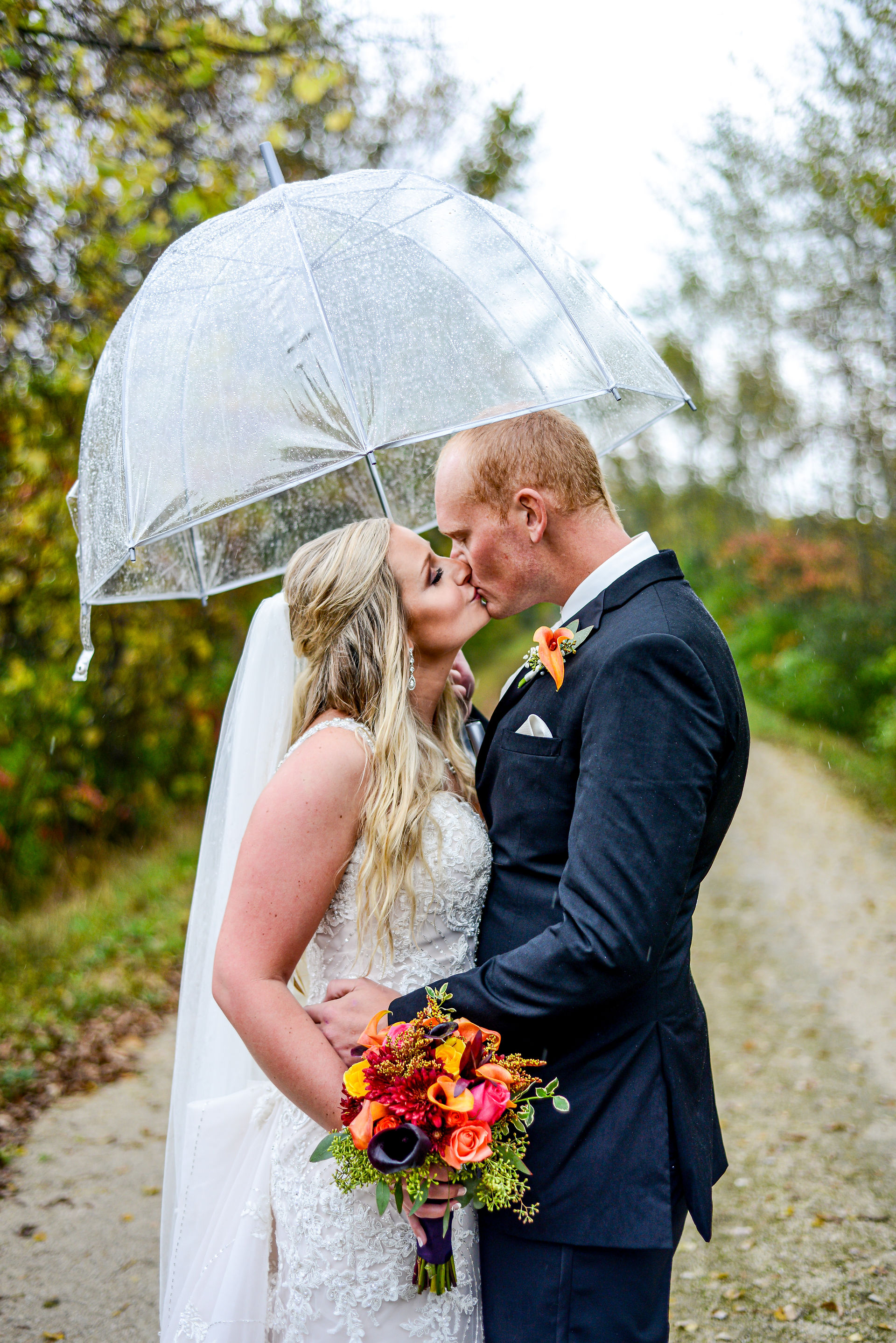 Bride and groom kiss under a clear umbrella on their rainy wedding day