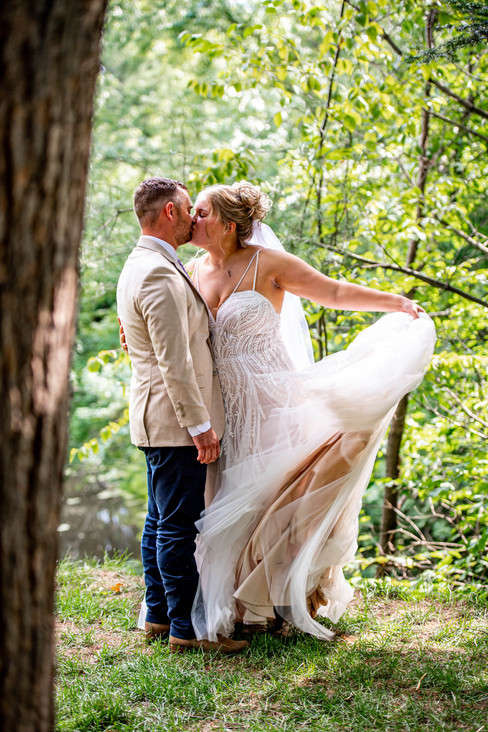 A bride and groom kiss in a lush forest. The bride tosses her dress in the wind for a dramatic photo
