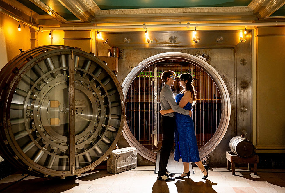 A couple in masquerade attire embraces inside an illuminated bank vault, with a massive metal door and industrial lighting in the background at Venue 404 in Oshkosh Wisconsin