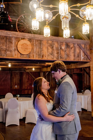 a couple shares their first dance at their wedding at a rustic venue. Springbrook events sign and a large chandelier visible in the background