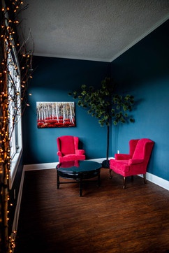 two red chairs placed in a corner create a relaxing spot to sit in a blue painted room. A fake tree and small lights on the window creating an inviting environment
