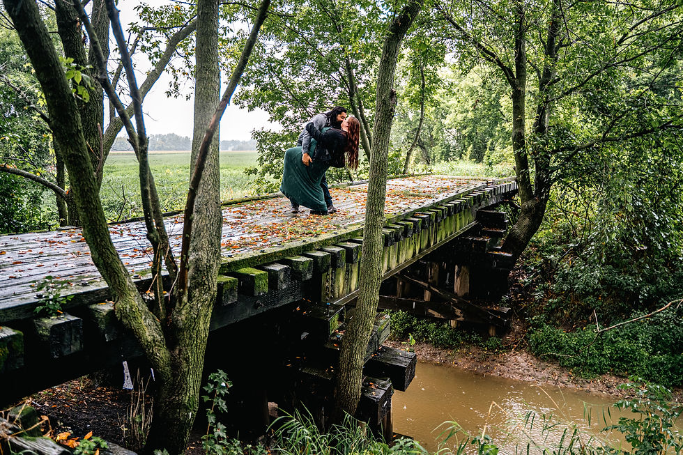 And engaged couple perform a dip and kiss on a bridge covered with moss crossing over a river in the woods. It is lightly raining out