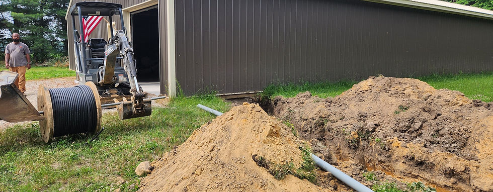 Open trench with gray conduit beside a pole barn, a mini excavator and a cable spool