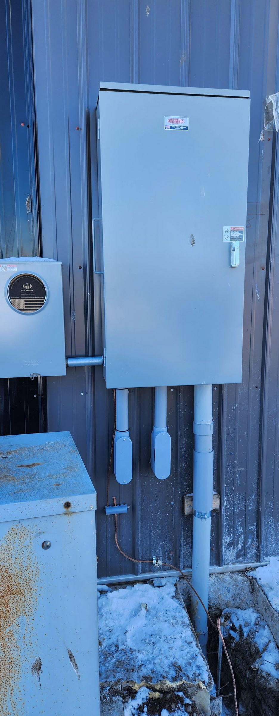 Closer view of a CT cabinet and meter socket on a metal building, with an old enclosure in front