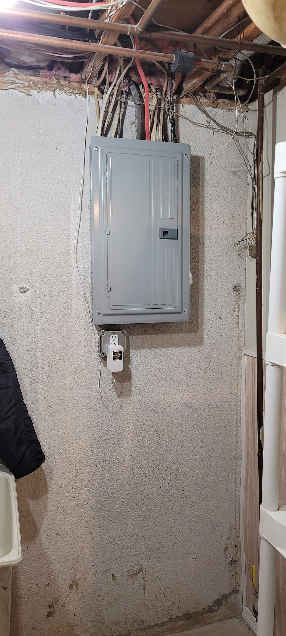 Finished new breaker panel with cover on, on a basement wall, with an outlet box below it