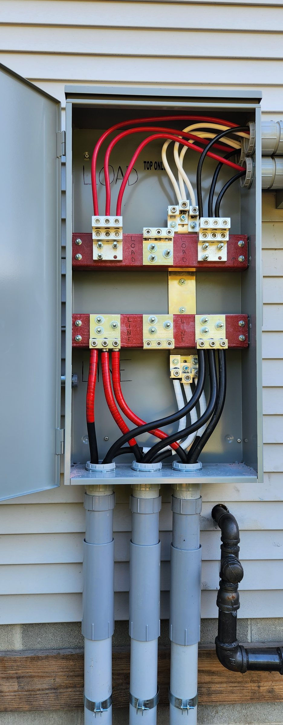 Open tap box with red bus blocks and conductors on gray siding, three conduits below