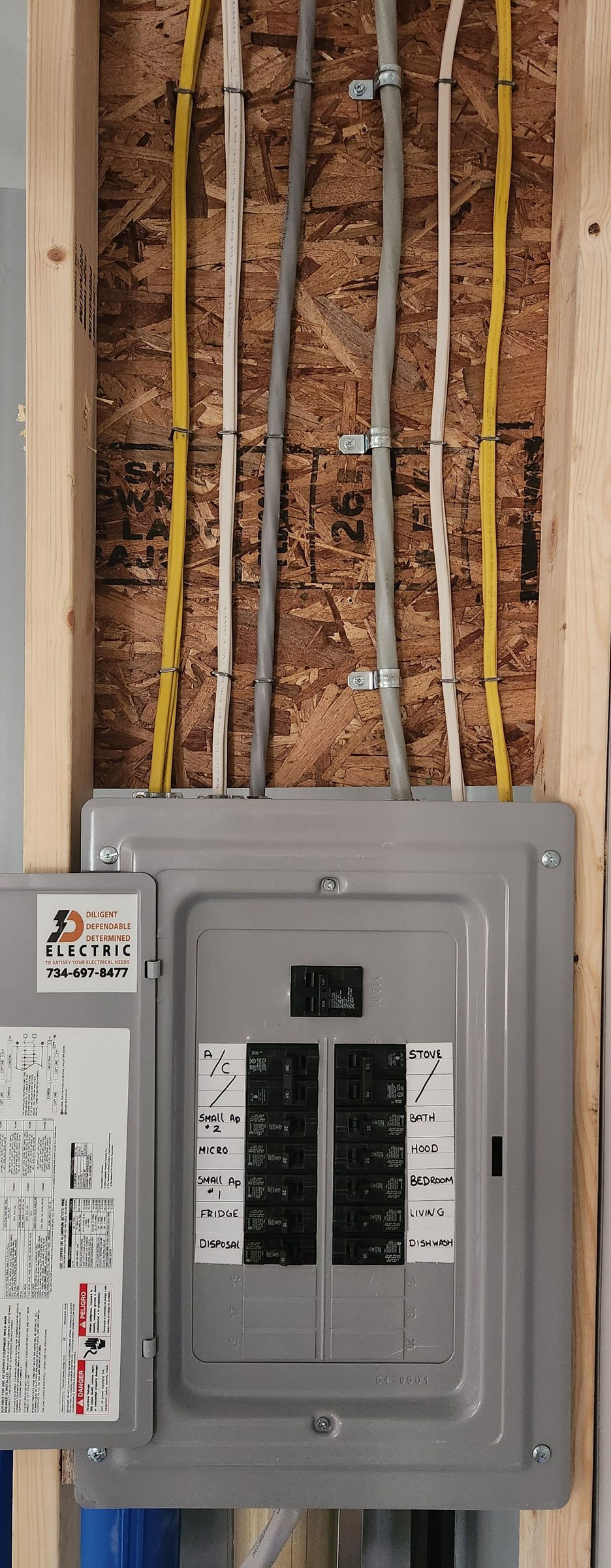New breaker panel with a 3D Electric sticker and hand-labeled circuits, neat cables stapled up the OSB wall above it