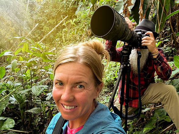 male with a long telephoto lens shooting rare birds in a colombian rainforest while the female companion takes a selfie of the moment
