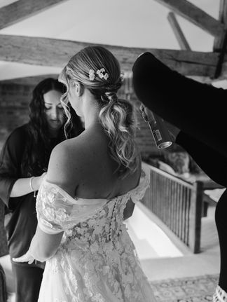 A black and white photo of a textured, wavy ponytail bridal hairstyle being sprayed with hairspray