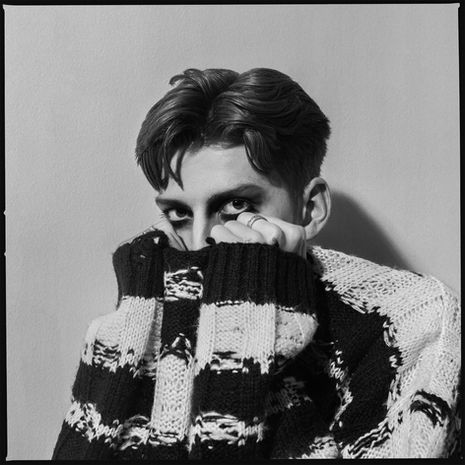 Man peaking over the hem of a loose knitted, stripped sweater he is holding close to his face
