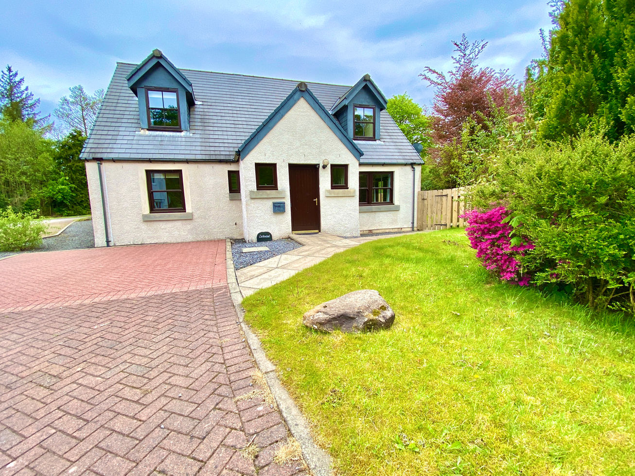 Light coloured detached house with grey roof and mono bloc driveway, and grass garden