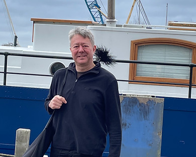 George, the Hart & Kohl chimney sweep, standing by a boat