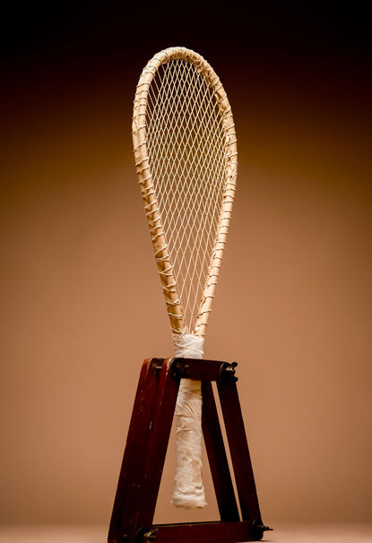 3D rendering of the Scaino‑type Scanno real tennis racquet shown in full profile, oriented to the left, with a warm photographic background