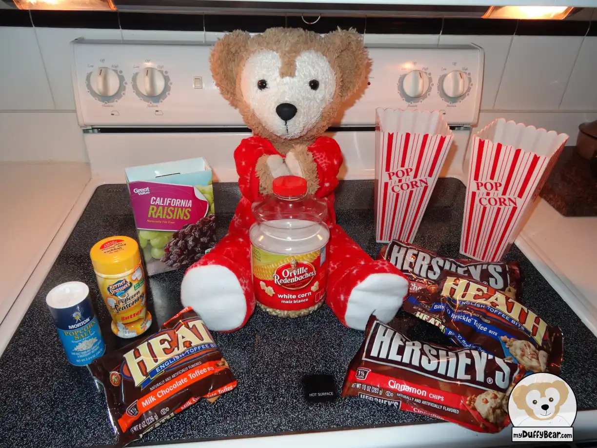 Duffy is holding one jar of Orville Redenbacher's popcorn and is surrounded by ingredients; such as a bag of Hershey’s Heath Chocolate chips, Hershey’s cinnamon, popcorn salt, a box of California Raisins for some of his Popcorn recipes