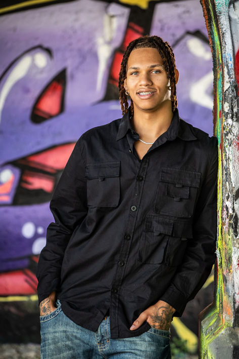 Young man in black shirt with a wall of colorful graffiti art behind him.