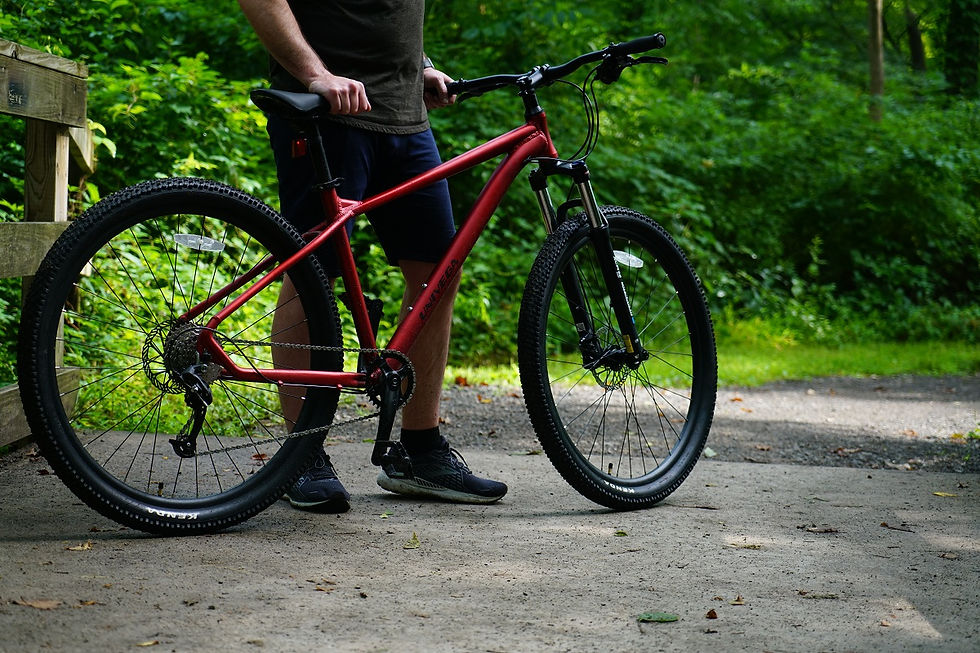 Person standing with a red mountain bike on a forest trail, surrounded by lush green trees and natural scenery.