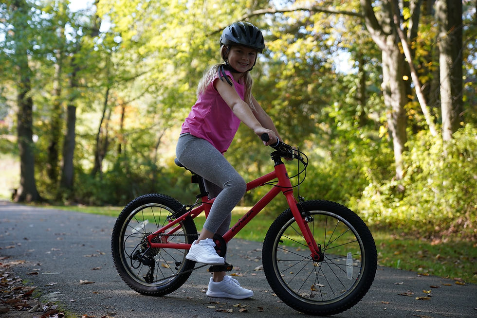 Young girl riding kids bicycle on wooded path with helmet, highlighting safe outdoor riding and family friendly bikes from Mendham