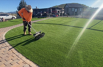 Crew member installing artificial turf beside a paver patio