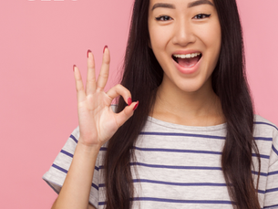Girl on a pink background making an "okay" sign with her hand. 