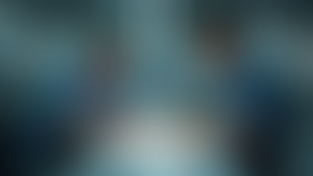 Two men in blue shirts work intently under a desk lamp, reviewing documents in a dimly lit office, creating a focused atmosphere.