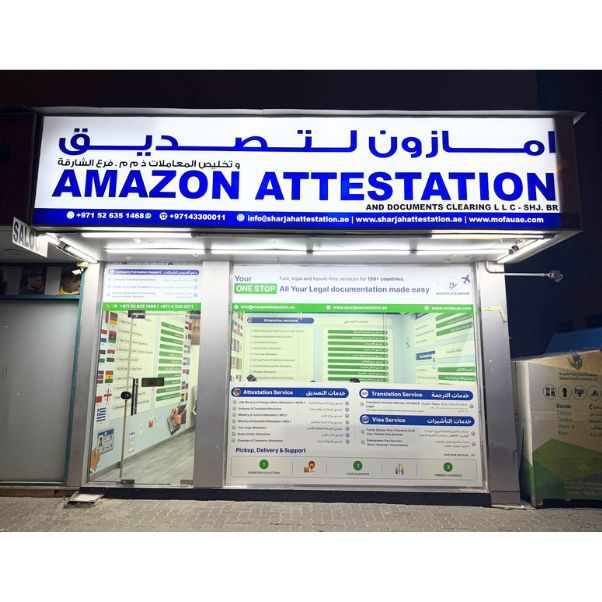 Storefront of Amazon Attestation at night, typing center Sharjah with bright signage in English and Arabic. Service details in the window display.