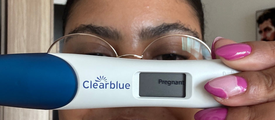 Charnè smiling while holding a Clearblue digital pregnancy test showing “Pregnant”.