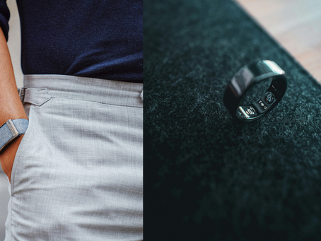 Person in a navy shirt with a gray whoop band device on their wrist, hand in pocket. A tech oura ring on a dark textured surface, no visible text.