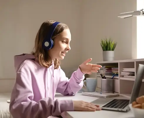 Teenager im VideoCall mit Kopfhörer auf vor einem Laptop am Schreibtisch sitzend