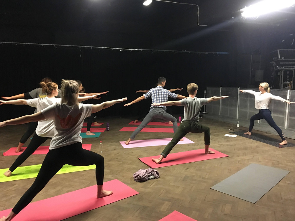 A group of students wearing active gear and standing on yoga matts, perform the warrior pose