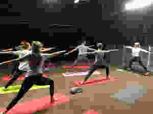 A group of students wearing active gear and standing on yoga matts, perform the warrior pose